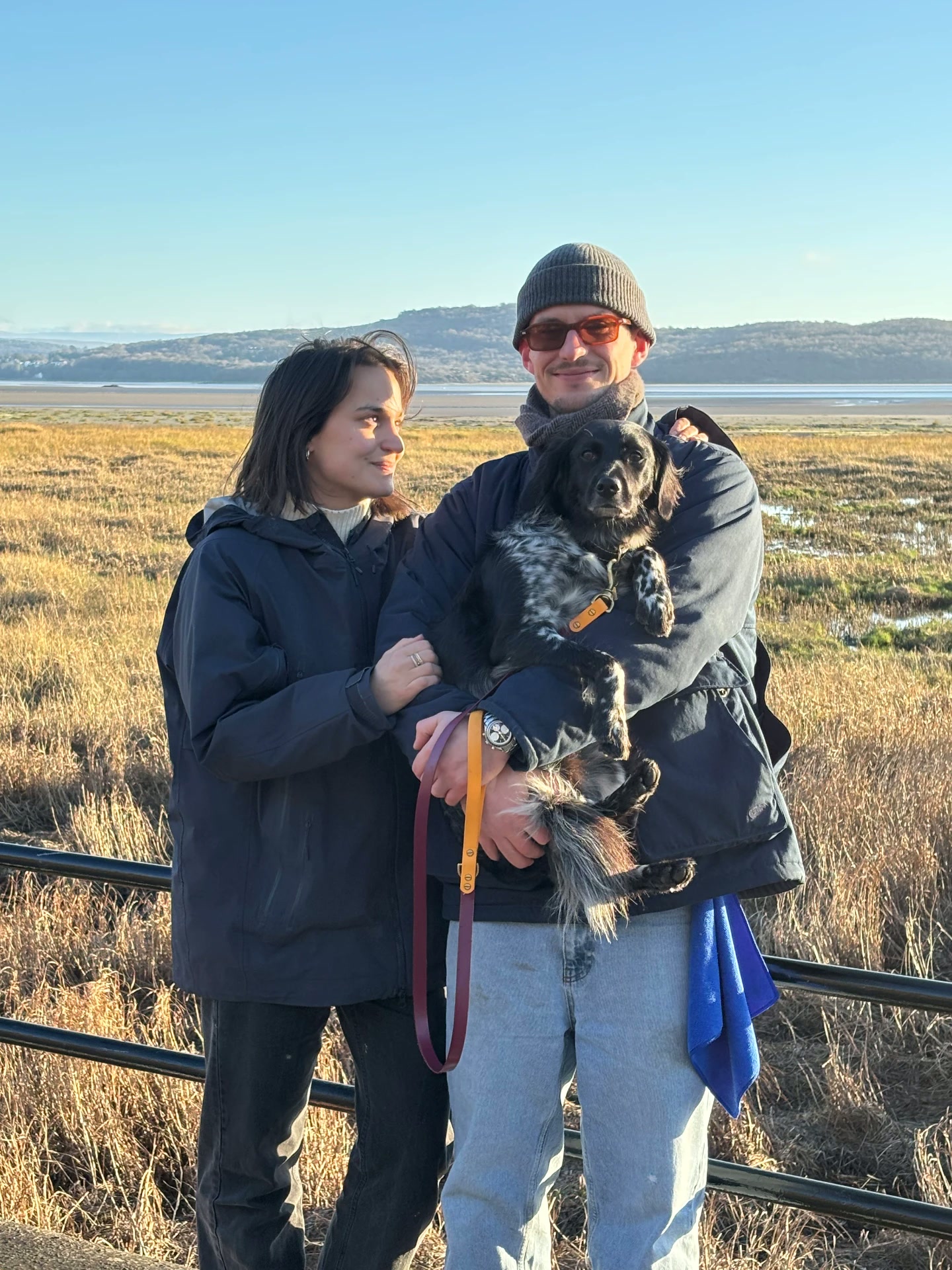 Zoe & Pete holding their dog in a coastal marsh